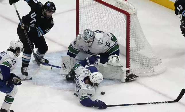 Utah Hockey Club center Alexander Kerfoot (15) looks on as Vancouver Canucks' goaltender Thatcher Demko (35) and Teddy Blueger (53) make a save against Utah Hockey Club during the first period of an NHL hockey game Wednesday, Dec. 18, 2024, in Salt Lake City. (AP Photo/Rick Bowmer)