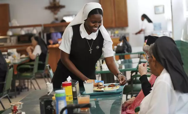 Sister Seyram Mary Adzokpa, of the Sisters of the Holy Family, brings a tray of food to an elderly sister at the motherhouse in New Orleans, Tuesday, June 25, 2024. (AP Photo/Jessie Wardarski)