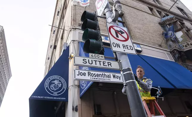 An SFMTA worker installs the Joe Rosenthal Way street sign to honor Rosenthal, who won the Pulitzer Prize for his iconic photo of U.S. Marines raising the flag on the Japanese island of Iwo Jima during WWII, Thursday, Dec. 12, 2024, in San Francisco. (AP Photo/Minh Connors)