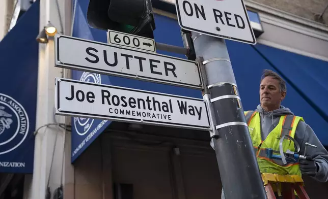 An SFMTA worker installs the Joe Rosenthal Way street sign to honor Rosenthal, who won the Pulitzer Prize for his iconic photo of U.S. Marines raising the flag on the Japanese island of Iwo Jima during WWII, Thursday, Dec. 12, 2024, in San Francisco. (AP Photo/Minh Connors)