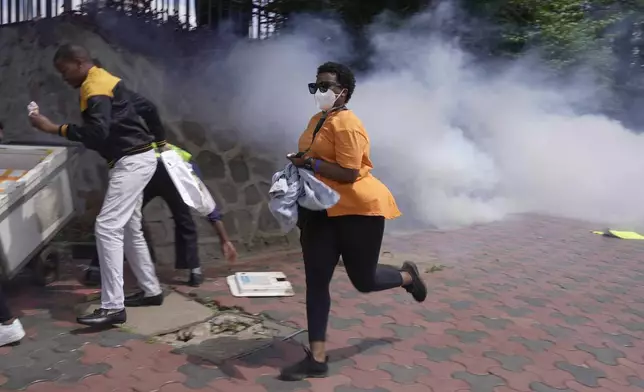 A woman runs from a cloud of tear gas fired by anti-riot police during the march against the rising cases of femicide, in downtown Nairobi, Kenya, Tuesday, Dec. 10, 2024. (AP Photo/Brian Inganga)