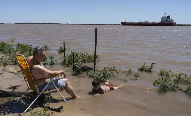 Briceno Medina and his grandfather Gerardo Medina relax on the banks of the Parana River in Villa Gobernador Galvez, Argentina, Wednesday, Dec. 4, 2024. (AP Photo/Rodrigo Abd)