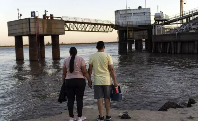 A couple watches the sun set outside an agricultural export port on the banks of the Parana River in Puerto General San Martin, Argentina, Monday, Dec. 2, 2024. (AP Photo/Rodrigo Abd)