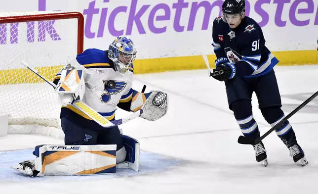 St. Louis Blues goaltender Joel Hofer (30) makes a save on a Winnipeg Jets shot as Cole Perfetti (91) looks for the rebound during the third period of their NHL hockey game in Winnipeg, Canada Tuesday, Dec. 3, 2024. (Fred Greenslade/The Canadian Press via AP)