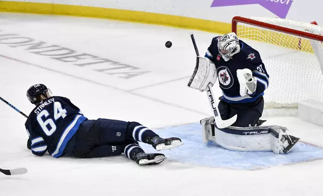 Winnipeg Jets goaltender Connor Hellebuyck (37) makes a save on a St. Louis Blues shot as Logan Stanley (64) slides in front of the net during the third period of their NHL hockey game in Winnipeg, Canada Tuesday, Dec. 3, 2024. (Fred Greenslade/The Canadian Press via AP)