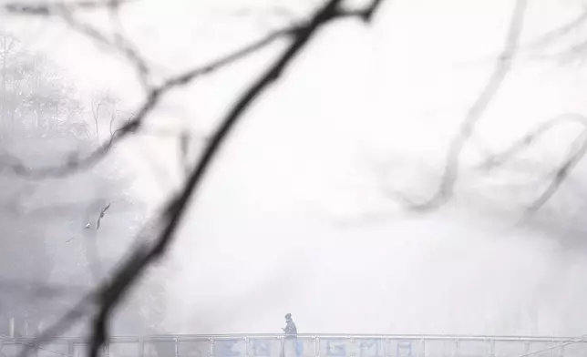 A man crosses a bridge shrouded by pollution haze as smog covers Sarajevo, Bosnia, Thursday, Dec. 19, 2024. (AP Photo/Armin Durgut)