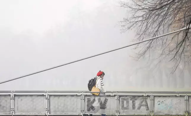 People cross a bridge shrouded by pollution haze as smog covers Sarajevo, Bosnia, Thursday, Dec. 19, 2024. (AP Photo/Armin Durgut)