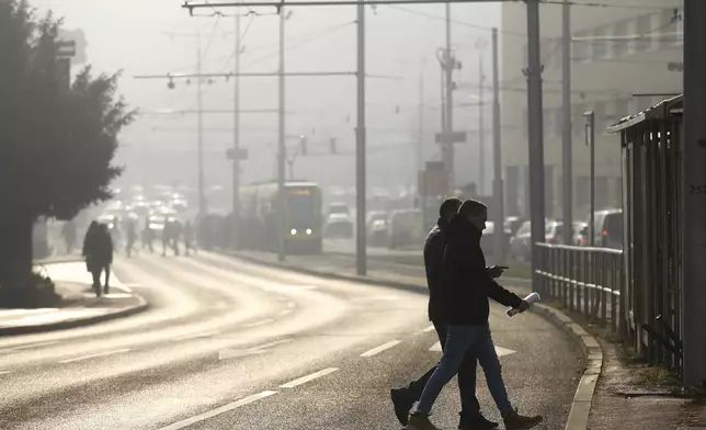 People cross the street shrouded by pollution haze as smog covers Sarajevo, Bosnia, Thursday, Dec. 19, 2024. (AP Photo/Armin Durgut)