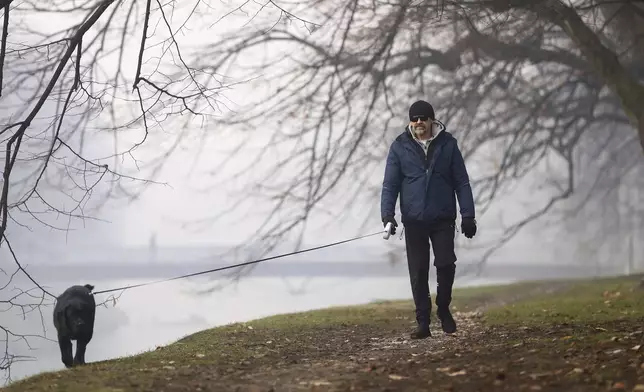 A man walks a dog shrouded by pollution haze as smog covers Sarajevo, Bosnia, Thursday, Dec. 19, 2024. (AP Photo/Armin Durgut)