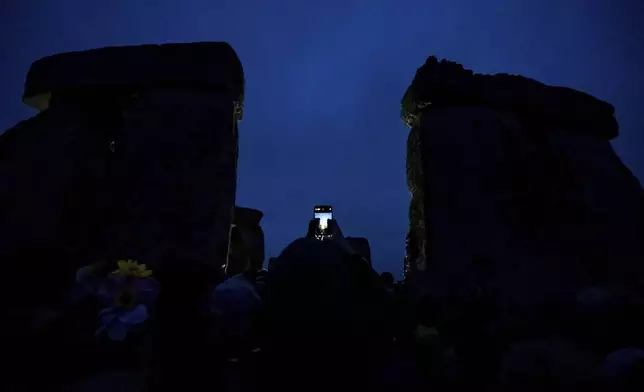 A person holds up a smart phone as they wait for sunrise during the winter Solstice celebrations at Stonehenge, England, Saturday, Dec. 21, 2024. (AP Photo/Anthony Upton)