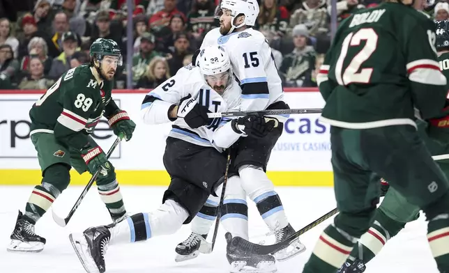 Utah Hockey Club center Jack McBain, middle left, shoots the puck as he collides with center Alexander Kerfoot (15) during the second period of an NHL hockey game against the Minnesota Wild Friday, Dec. 20, 2024, in St. Paul, Minn. (AP Photo/Matt Krohn)