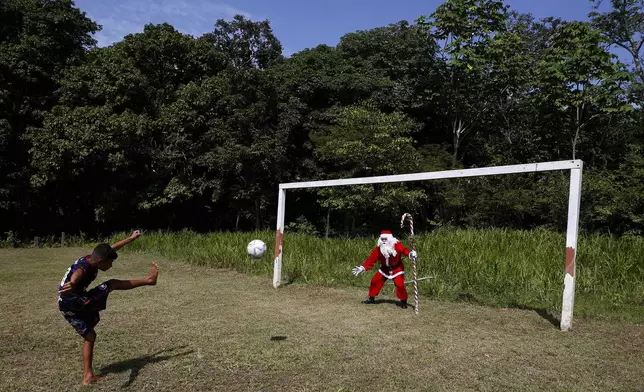 A young Amazonian resident strikes a ball towards Jorge Barroso, dressed as Santa Claus, who gave the ball to the boy after Barroso arrived on a boat to distribute Christmas gifts to children, in Iranduba, Brazil, Saturday, Dec. 21, 2024. (AP Photo/Edmar Barros)