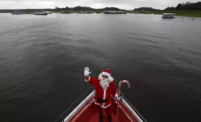 Jorge Barroso, dressed as Santa Claus, waves as he arrives on a boat to distribute Christmas gifts to children who live in the riverside communities of the Amazon, in Iranduba, Brazil, Saturday, Dec. 21, 2024. (AP Photo/Edmar Barros)