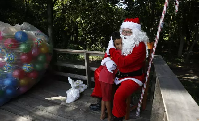 Jorge Barroso, dressed as Santa Claus, is embraced by a young resident after arriving on a boat to distribute Christmas gifts to children who live in the riverside communities of the Amazon, in Iranduba, Brazil, Saturday, Dec. 21, 2024. (AP Photo/Edmar Barros)