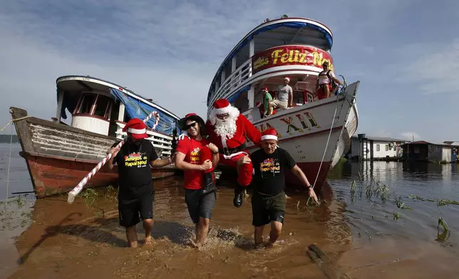 Jorge Barroso, dressed as Santa Claus, is carried by his helpers after arriving on a boat to distribute Christmas gifts to children who live in the riverside communities of the Amazon, in Iranduba, Brazil, Saturday, Dec. 21, 2024. (AP Photo/Edmar Barros)