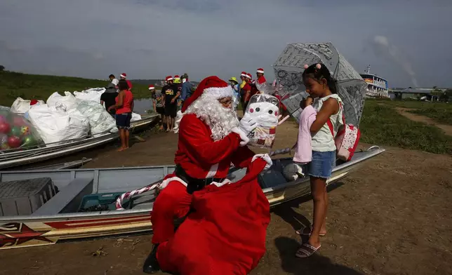 Jorge Barroso, dressed as Santa Claus, presents a gift to a young resident after arriving on a boat to distribute Christmas gifts to children who live in the riverside communities of the Amazon, in Iranduba, Brazil, Saturday, Dec. 21, 2024. (AP Photo/Edmar Barros)