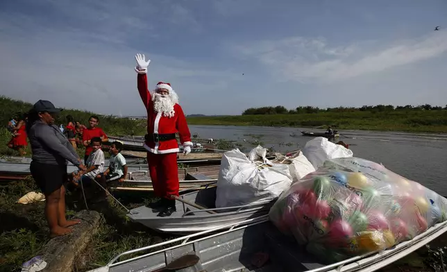 Jorge Barroso, dressed as Santa Claus, waves as he arrives on a boat to distribute Christmas gifts to children who live in the riverside communities of the Amazon, in Iranduba, Brazil, Saturday, Dec. 21, 2024. (AP Photo/Edmar Barros)