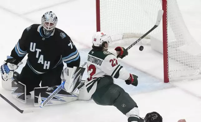 Minnesota Wild center Marat Khusnutdinov, center, scores against Utah Hockey Club goaltender Karel Vejmelka (70) during the second period of an NHL hockey game Tuesday, Dec. 10, 2024, in Salt Lake City. (AP Photo/Rick Bowmer)