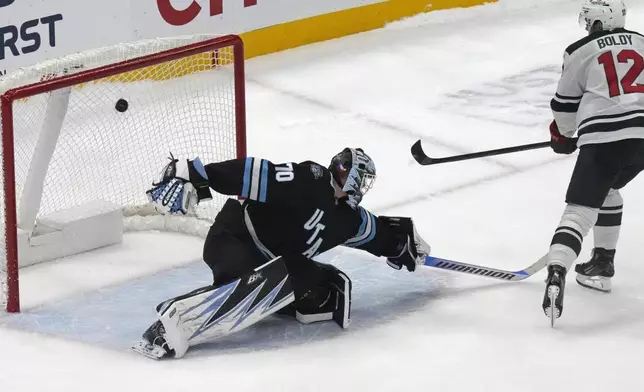 Minnesota Wild left wing Matt Boldy (12) scores against Utah Hockey Club goaltender Karel Vejmelka (70) during the shootout of an NHL hockey game Tuesday, Dec. 10, 2024, in Salt Lake City. (AP Photo/Rick Bowmer)