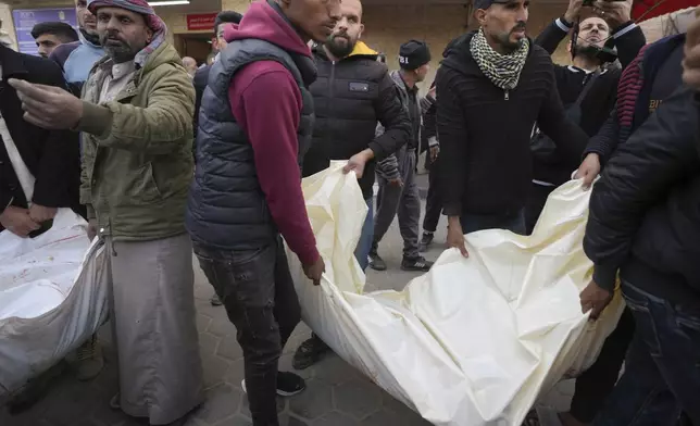 Palestinians carry white sacks containing the bodies of those killed in overnight Israeli airstrikes on the Maghazi refugee camp, at Al-Aqsa Hospital, in Deir al-Balah, central Gaza Strip, Saturday, Dec. 28, 2024. (AP Photo/Abdel Kareem Hana)