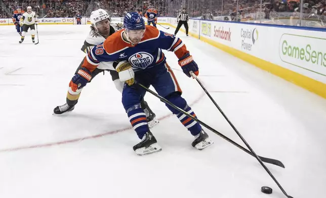 Vegas Golden Knights' Noah Hanifin (15) and Edmonton Oilers' Zach Hyman (18) battle for the puck during the second period of an NHL game in Edmonton, Alberta, Saturday, Dec. 14, 2024. (Jason Franson/The Canadian Press via AP)