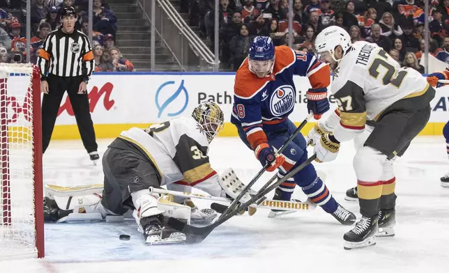 Vegas Golden Knights goalie Adin Hill (33) is scored on by Edmonton Oilers' Zach Hyman (18) and Shea Theodore (27) defends during the second period of an NHL game in Edmonton, Alberta, Saturday, Dec. 14, 2024. (Jason Franson/The Canadian Press via AP)