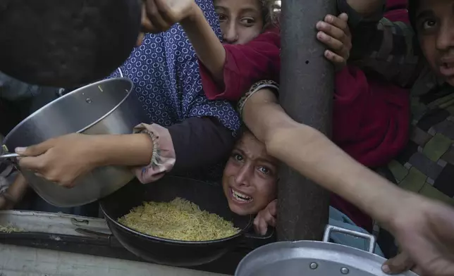 A Palestinian girl struggles to reach for food at a distribution center in Khan Younis, Gaza Strip Friday, Dec. 6, 2024. (AP Photo/Abdel Kareem Hana)