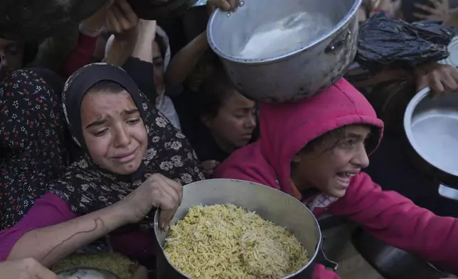 Palestinian girls struggle to reach for food at a distribution center in Khan Younis, Gaza Strip Friday, Dec. 6, 2024. (AP Photo/Abdel Kareem Hana)