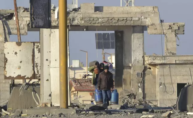 People carry bottles of butane gas, as they cross the destroyed crossing border point between Lebanon and Syria which hit by an Israeli airstrike, in Arida, north Lebanon, Friday, Dec. 6, 2024. (AP Photo)