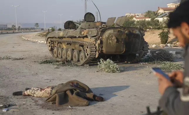 The body of a government soldier lies next to a armoured vehicle in a street in the aftermath of the opposition's takeover of Hama, Syria, Friday, Dec. 6, 2024. (AP Photo/Ghaith Alsayed)