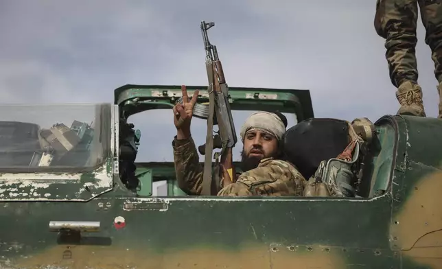 A Syrian opposition fighter sits on the cockpit of a Syrian airforce plane as he poses flashing the victory sign at the Hama military airport, Syria, Friday Dec. 6, 2024. (AP Photo/Ghaith Alsayed)