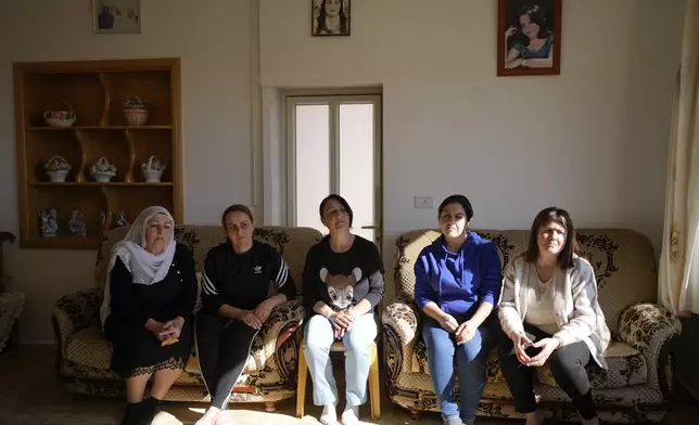 Five of six Safadi sisters sit on a couch under a portrait of their sister, Sawsan, who lives inside the buffer zone near the "Alpha Line" that separates the Israeli-controlled Golan Heights from Syria, in the town of Majdal Shams, Wednesday, Dec. 18, 2024. (AP Photo/Matias Delacroix)