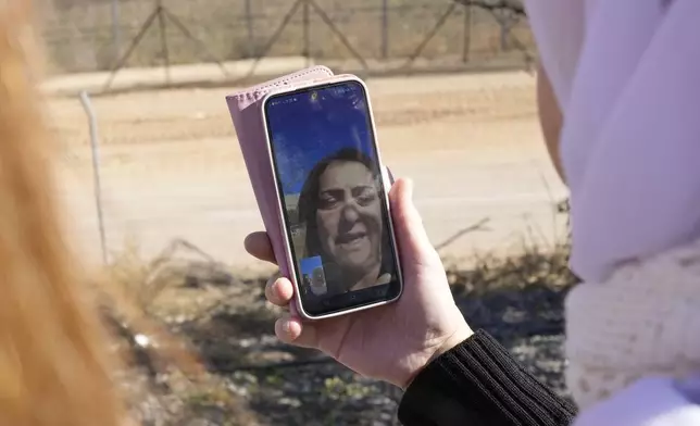 Samar Safadi holds her phone as she talks by video call with her sister, Sawsan, who lives inside the buffer zone near the "Alpha Line" that separates the Israeli-controlled Golan Heights from Syria, in the town of Majdal Shams, Wednesday, Dec. 18, 2024. (AP Photo/Matias Delacroix)