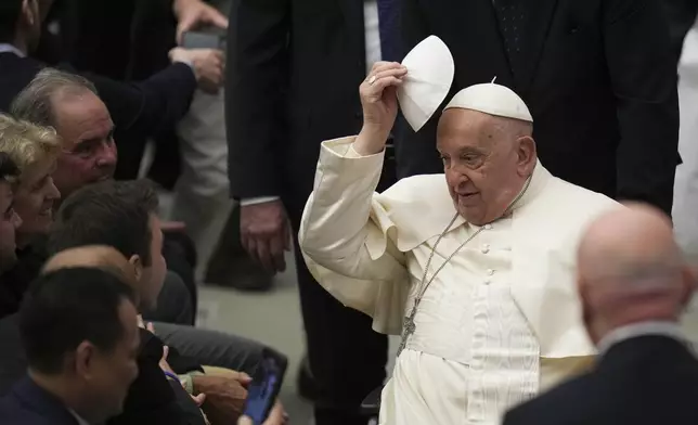 Pope Francis tries a skullcap received by faithful during the weekly general audience at the Vatican, Wednesday, Dec. 18, 2024. (AP Photo/Alessandra Tarantino)