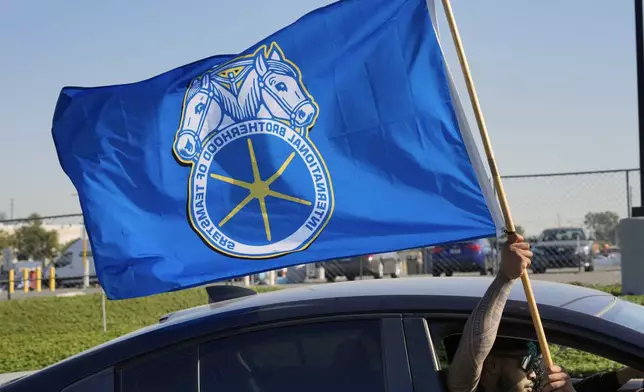 A supporter waving a Teamster flag rides past Amazon workers striking outside the gates of an Amazon Fulfillment Center on Friday, Dec. 20, 2024, in City of Industry, Calif. (AP Photo/Damian Dovarganes)