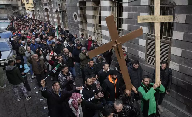 Syrian Christians carry crosses and shout slogans in Damascus, Syria, Tuesday, Dec. 24, 2024, as they march during a protest after a Christmas tree was set on fire in Hamah city on Sunday. (AP Photo/Hussein Malla)