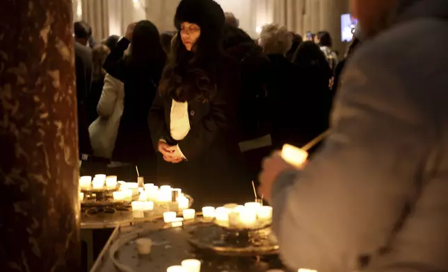 A woman prays by candles at Notre Dame Cathedral as the monument hosts Christmas Eve services for the first time since a devastating 2019 fire, Tuesday, Dec. 24, 2024 in Paris. (AP Photo/Thomas Padilla)