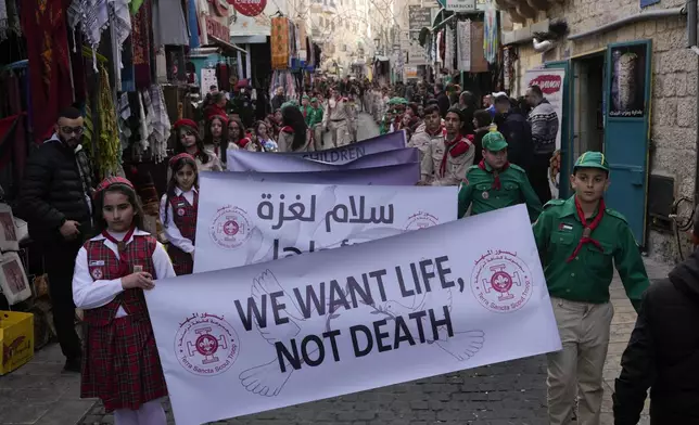 Scouts hold a sign that reads "We want life, not death" during the traditional Christian procession towards the Church of the Nativity, traditionally believed to be the birthplace of Jesus, on Christmas Eve, in the West Bank city of Bethlehem, Tuesday, Dec. 24, 2024. (AP Photo/Matias Delacroix)