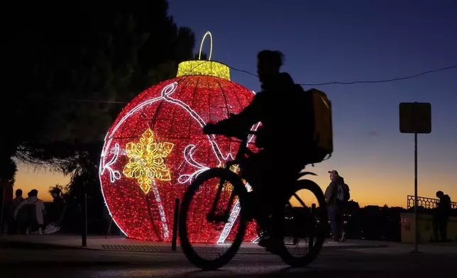 A delivery rider cycles past Christmas decorations in Lisbon, Tuesday, Dec. 24, 2024. (AP Photo/Armando Franca)