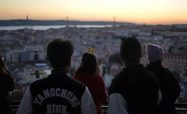 A woman wearing reindeer antlers watches the sun set from the Our Lady of the Hill viewpoint overlooking Lisbon, Tuesday, Dec. 24, 2024. (AP Photo/Armando Franca)