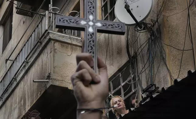 A woman looks at Syrian Christians carrying crosses and shouting slogans in Damascus, Syria, Tuesday, Dec. 24, 2024, during a protest after a Christmas tree was set on fire in Hamah city on Sunday. (AP Photo/Hussein Malla)