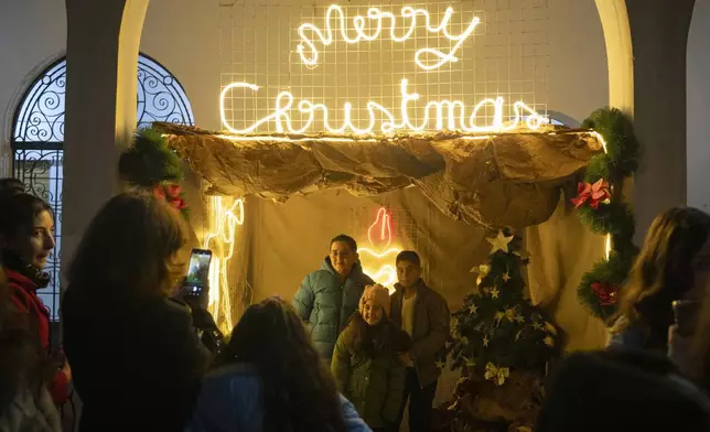 People pose for the photo next to Christmas decoration after attending a Christmas mass at the church of St. George, in Maaloula, some 60 km northern Damascus, Syria, Tuesday, Dec. 24, 2024. (AP Photo/Leo Correa)