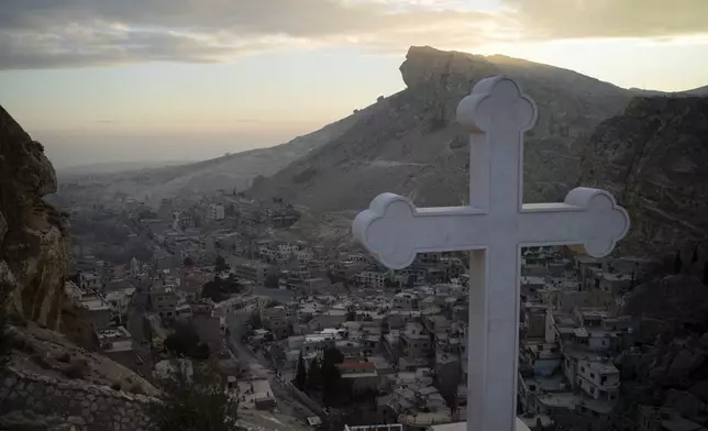 Houses are seen along the mountain as a cross stands over the Greek Orthodox convent Saint Takla on Christmas Eve in Maaloula, some 60 km northern Damascus, Syria, Tuesday, Dec. 24, 2024. (AP Photo/Leo Correa)