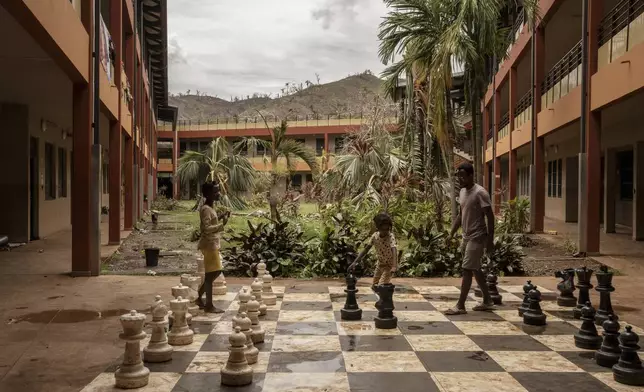 People interact by an outdoor chess board, after finding refuge at the Lycée des Lumières after losing their homes, in Mamoudzou, Mayotte, Thursday, Dec. 19, 2024. (AP Photo/Adrienne Surprenant)