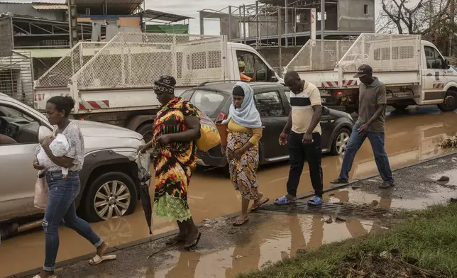 People walk along partially flooded roads, in Mamoudzou, Mayotte, Thursday, Dec. 19, 2024. (AP Photo/Adrienne Surprenant)