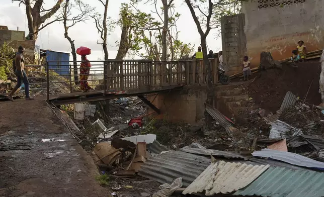 People walk past debris in the Kaweni slum Thursday, Dec. 19, 2024, on the outskirts of Mamoudzou, in the French Indian Ocean island of Mayotte, after Cyclone Chido. (AP Photo/Adrienne Surprenant)