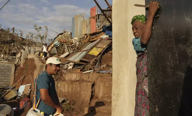 People walk past debris in the Kaweni slum Thursday, Dec. 19, 2024, on the outskirts of Mamoudzou, in the French Indian Ocean island of Mayotte, after Cyclone Chido. (AP Photo/Adrienne Surprenant)