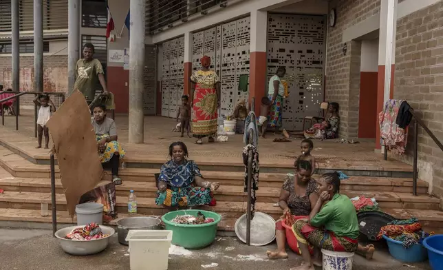 Women wash clothes after a short rain filled their pots with water, at the Lycée des Lumières where they found shelter after losing their homes, in Mamoudzou, Mayotte, Thursday, Dec. 19, 2024 . (AP Photo/Adrienne Surprenant)