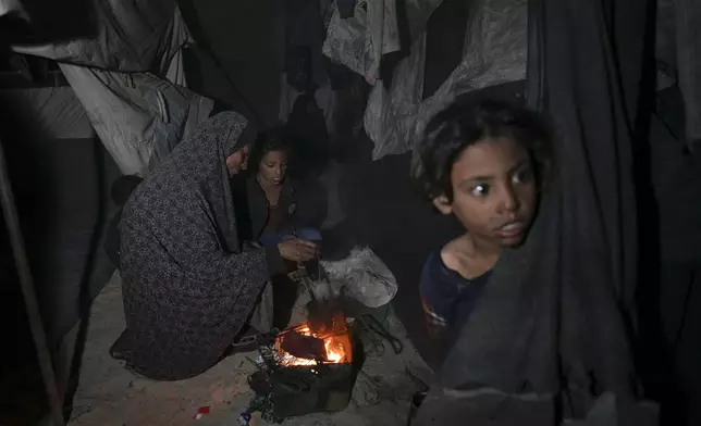 Shireen Daifallah, who was displaced with her children from northern Gaza, checks the fire next to their tent at a camp for displaced people in Deir al-Balah. Gaza Strip, Saturday, Nov. 30, 2024. (AP Photo/Abdel Kareem Hana)