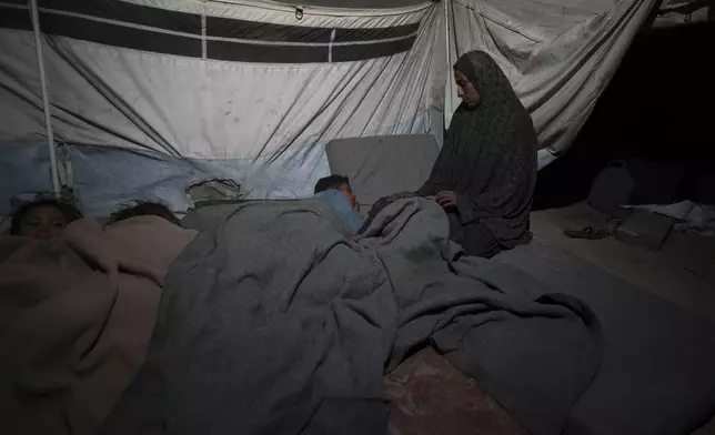 Shireen Daifallah, who was displaced from northern Gaza, checks one of her children in their tent at a camp for displaced people in Deir al-Balah. Gaza Strip, Saturday, Nov. 30, 2024. (AP Photo/Abdel Kareem Hana)